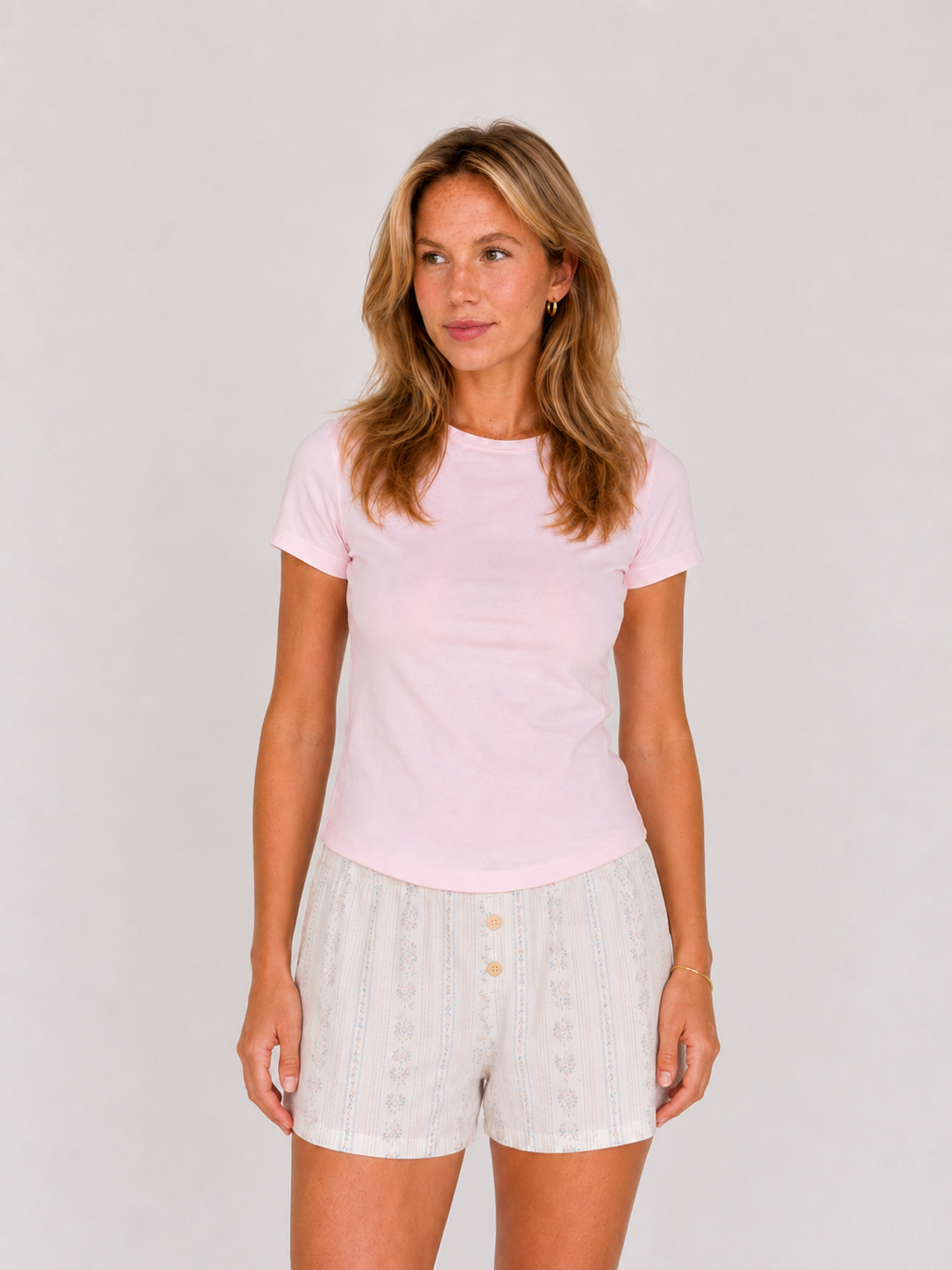 Woman wearing a light pink t-shirt and white shorts on a plain background